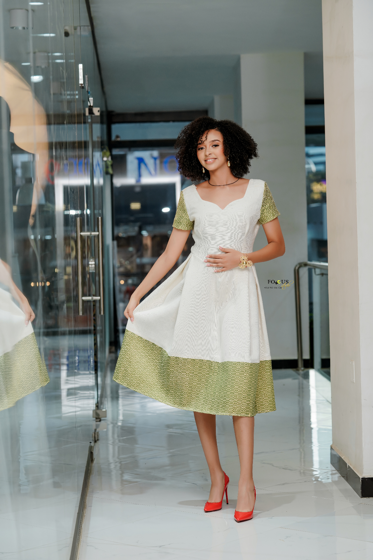 A model wearing an ivory dress with green woven Ethiopian trim and red heels