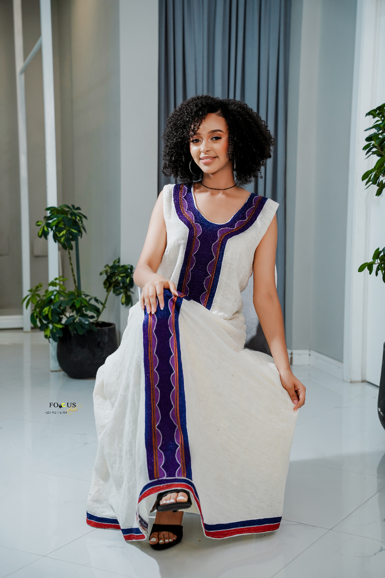 A model wearing a white traditional habesha dress with a vibrant purple and orange tilet