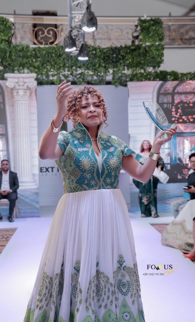 Sara Mohamed on the runway in a couture gown with a teal and gold embroidered bodice and ivory tulle skirt